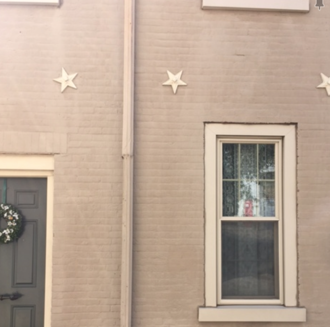 Brick Rowhome painted tan with cream colored star bolts and green door 