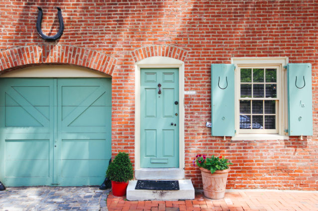 photo of a philadelphia rowhome with a matching teal door, shutters and garage. Two planters sit side by side by the main door to the home.