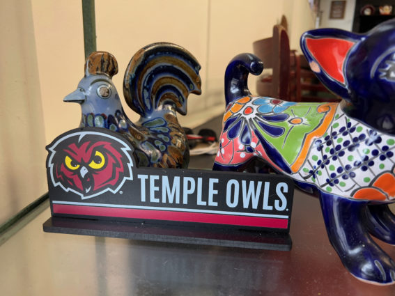 A close up of a sign promoting the temple owls alongside two mexican ceramic figurines