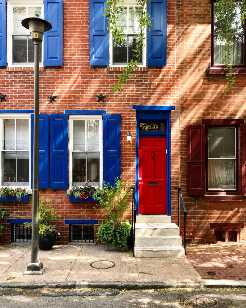 A brightly painted door, shutters, and planters add curb appeal to a brick Philly rowhome.